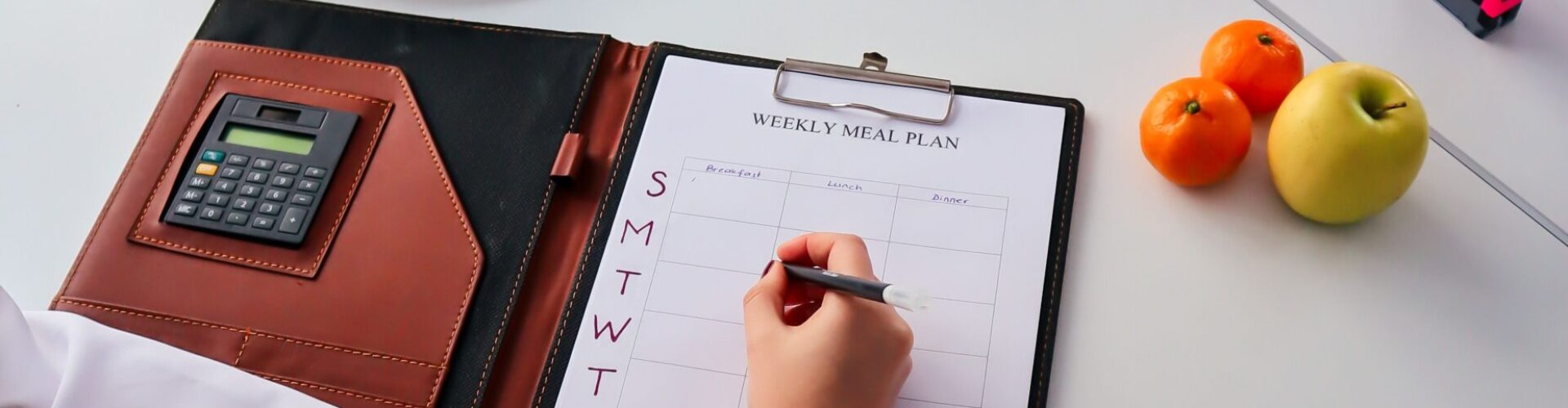 A nutritionist writes a weekly meal plan for a client in an office setting, surrounded by fresh fruits.